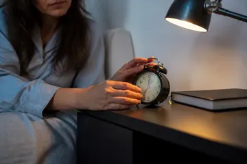 Masa lambasının altında bir kadının eli, masanın üzerindeki çalar saati ayarlıyor